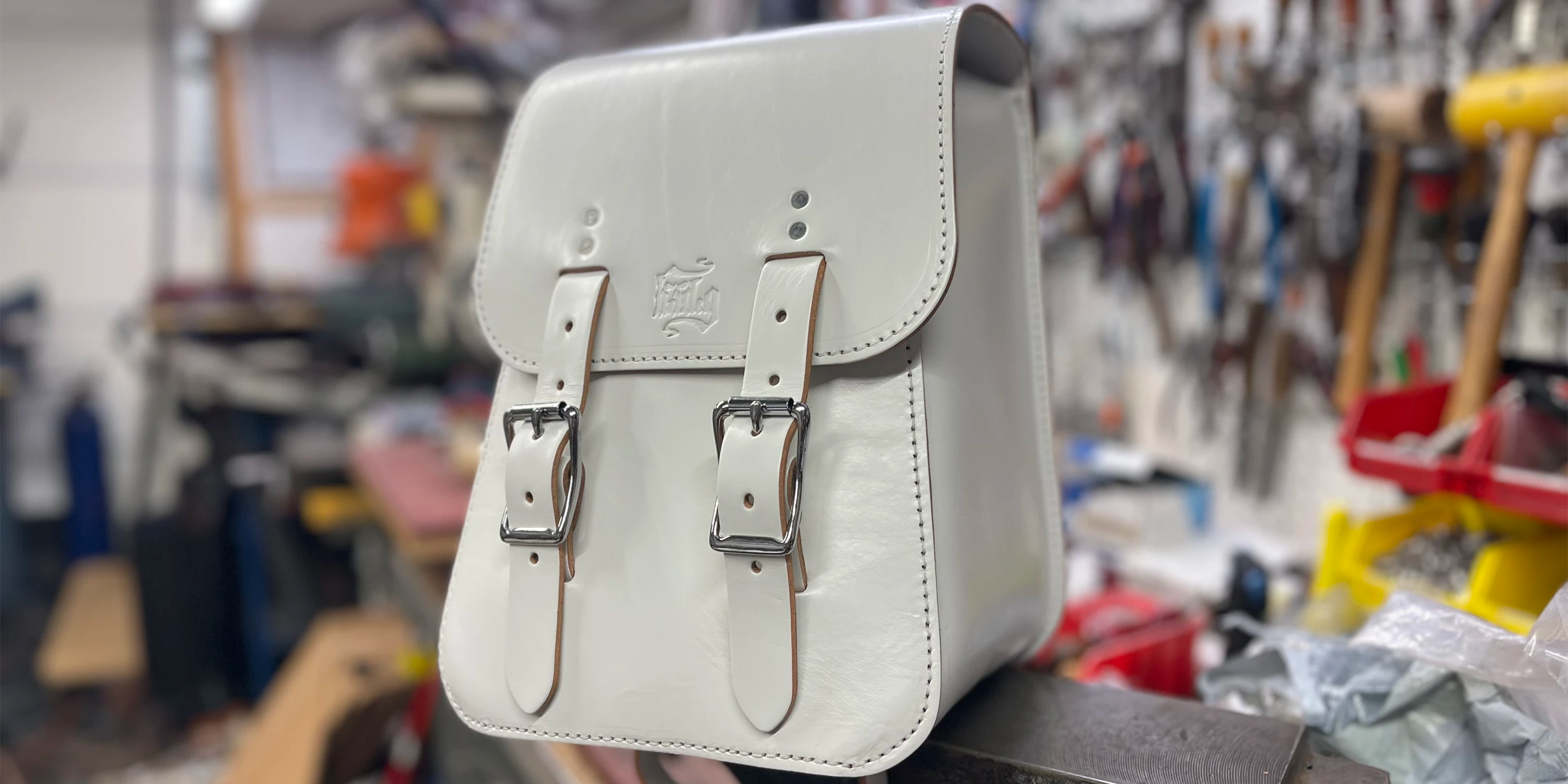 White leather satchel bag on a stand with a workshop background