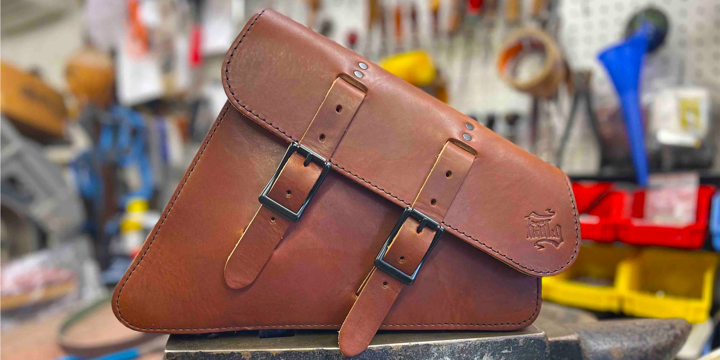Brown leather saddlebag with metal buckles on a workbench in a workshop.