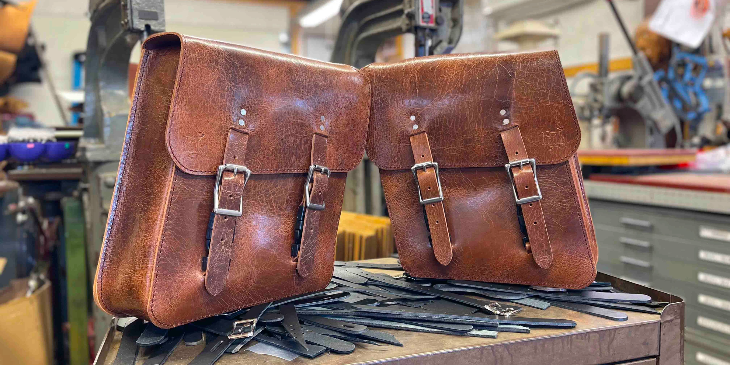 Two brown leather bags with buckles on a workbench in a workshop.